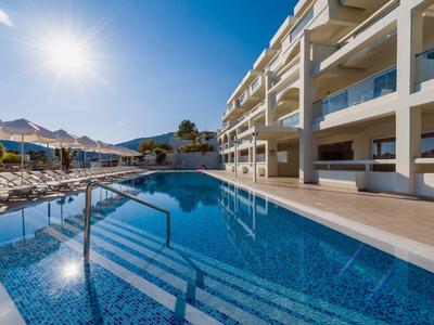 Moderner Hotelpool mit klar blauem Wasser, Sonnenliegen und sonnigem Himmel im Hintergrund.