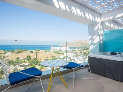 Balkon z jacuzzi, niebieskimi poduszkami na krzesłach i widokiem na morze w słoneczny dzień.