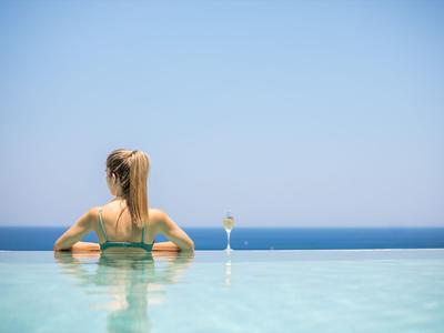 Frau im Pool mit Blick auf das Meer und einem Cocktailglas am Rand.