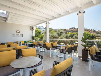 Offene Terrasse mit Sitzgelegenheiten und gelben Kissen mit Blick auf grüne Hügel.
