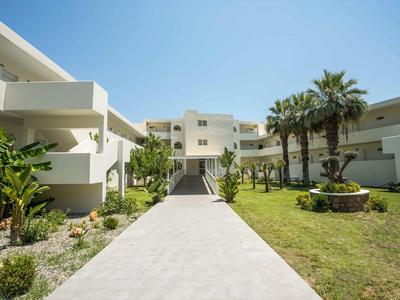 Moderner weißer Hotelkomplex mit Palmen und gepflegtem Garten unter blauem Himmel.
