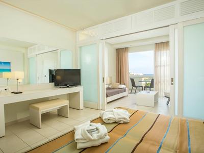 Jasny pokój hotelowy z łóżkiem podwójnym, telewizorem i balkonem z widokiem na morze.