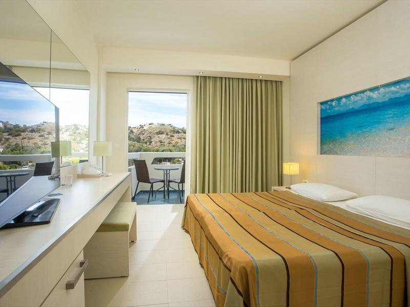 Nowoczesny pokój hotelowy z łóżkiem podwójnym, telewizorem, balkonem i widokiem na góry.