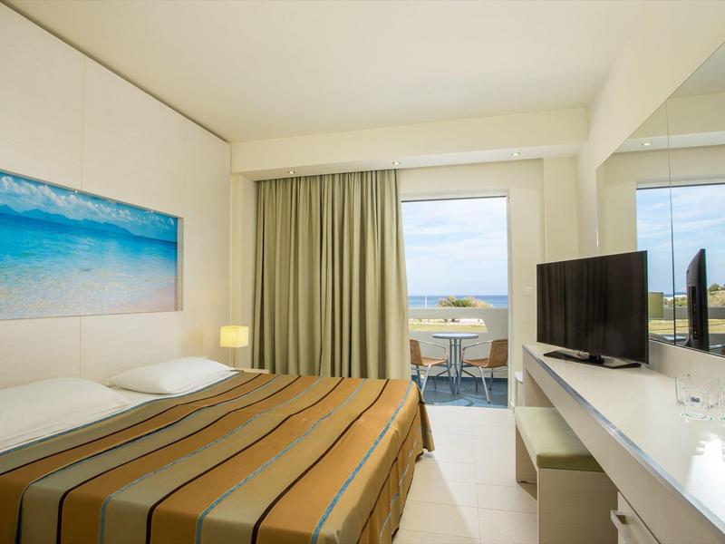 Nowoczesny pokój hotelowy z łóżkiem podwójnym, telewizorem i balkonem z widokiem na morze.