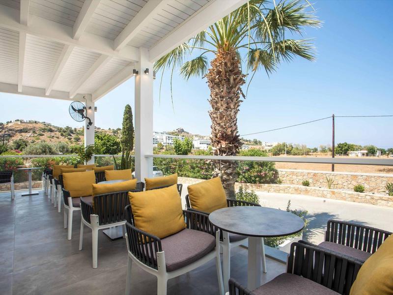 Zadaszony taras z stołami i krzesłami, widok na palmy i krajobraz