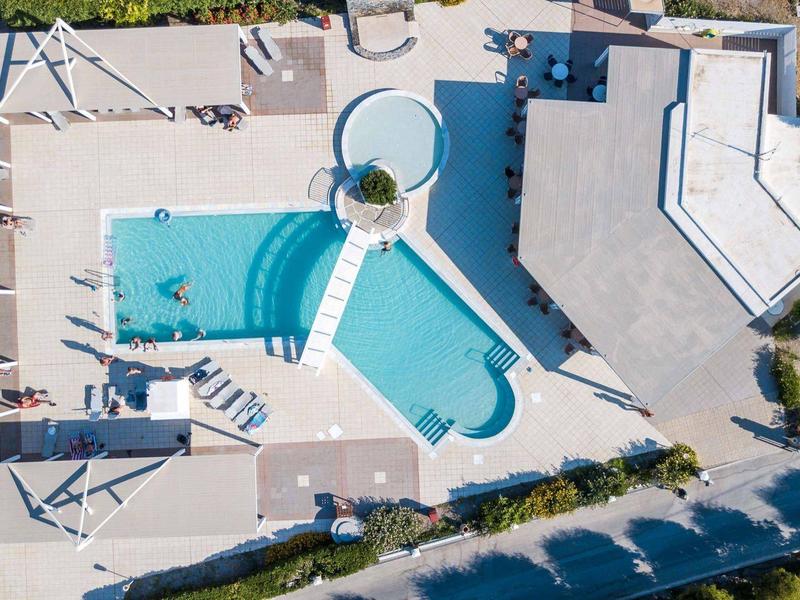 Widok z lotu ptaka na basen z leżakami i budynek otoczony drzewami i ścieżkami.