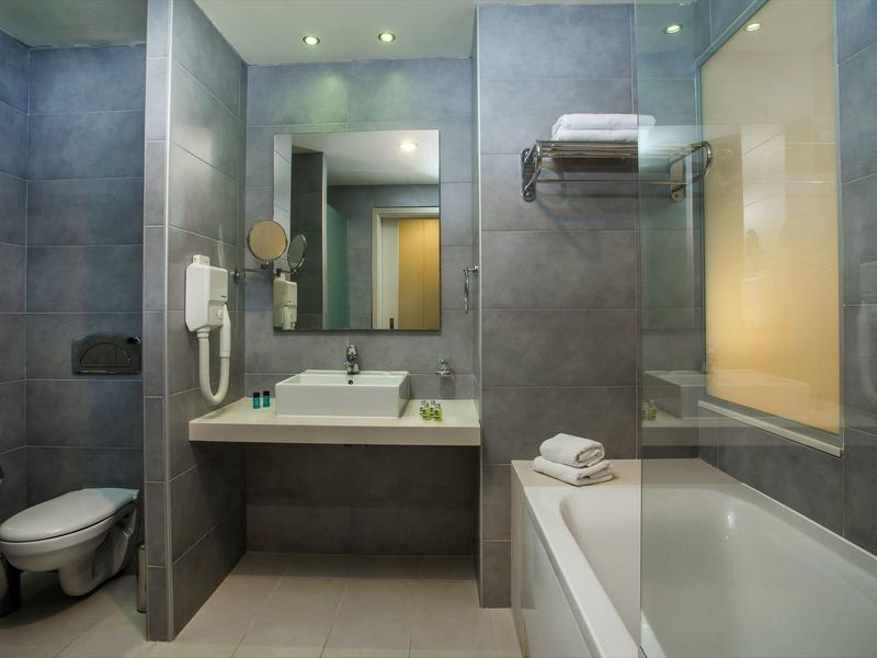 Nowoczesna łazienka hotelowa z toaletą, umywalką, dużym lustrem i wanną z ręcznikami.