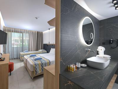 Habitación de hotel moderna con cama doble y baño elegante con espejo iluminado.