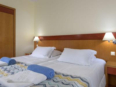 Habitación de hotel con dos camas individuales, cojines cómodos y toallas azules sobre cada colchón.