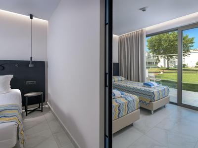 Habitación de hotel moderna con dos camas individuales y acceso a terraza con vista a césped y edificios.