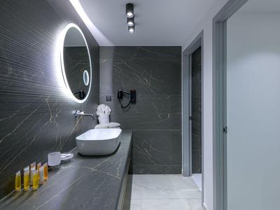 Baño moderno con espejo redondo iluminado y lavabo en un hotel.