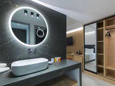 Baño moderno de hotel con espejo iluminado redondo y armario abierto.