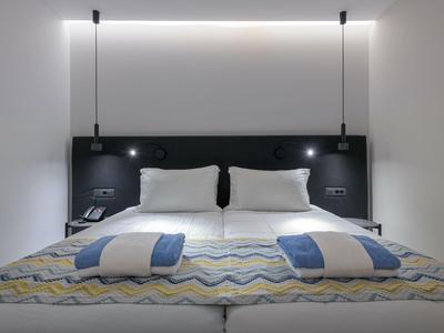 Habitación de hotel moderna con cama doble grande, dos almohadas, mantas y luces de lectura en la pared.