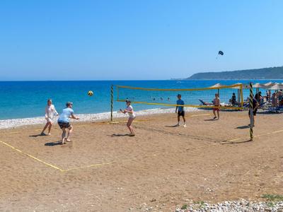 Personas jugando voleibol en una playa de arena bajo un cielo azul con el mar de fondo.
