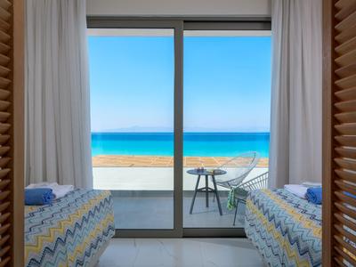 Habitación con dos camas con vista a la terraza y el mar en un día soleado.