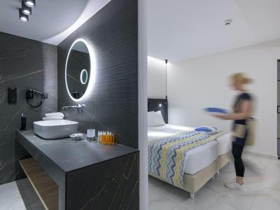 Habitación de hotel moderna con baño, espejo iluminado y cama bien hecha.