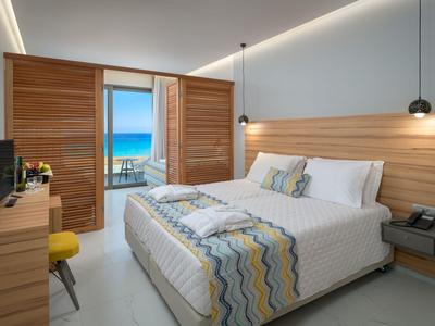Habitación de hotel moderna con cama doble, detalles de madera y vista al mar desde ventanas al balcón.