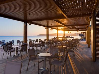 Terraza de hotel con mesas y sillas junto al mar al atardecer.