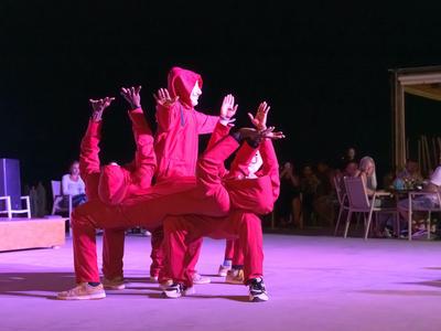 Cuatro personas con trajes rojos realizan una pose coreografiada en un escenario frente a un público.