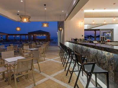 Nowoczesny bar hotelowy z ladą i stołkami, otwarty taras z stołami o zmierzchu.