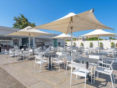 Teren zewnętrzny z białymi stolikami i krzesłami pod dużymi parasolami słonecznymi w słoneczny dzień.