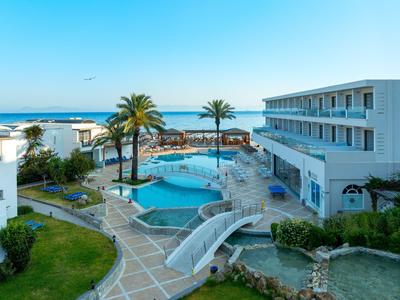 Hotel con gran piscina, palmeras y vista al mar bajo un cielo azul despejado.