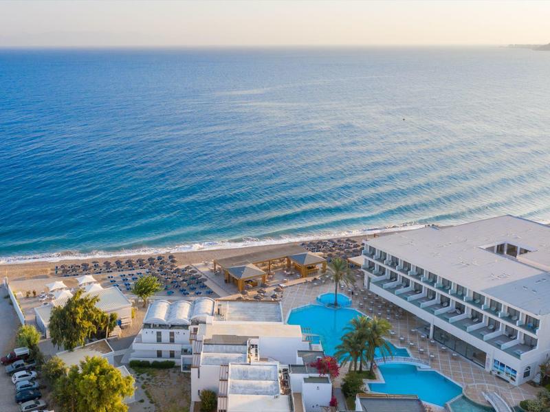 Luftaufnahme eines Hotels mit Pools am Strand, türkisblauem Meer und klarem Himmel.