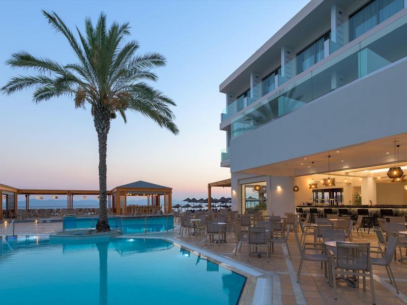 Moderner Hotelpool mit Palmen, Tischen und Stühlen, bei Sonnenuntergang am Meer.