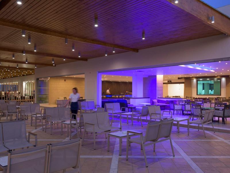 Moderner Innenraum mit Stühlen, Tischen und indirekter blauer Beleuchtung unter Holzdecke.