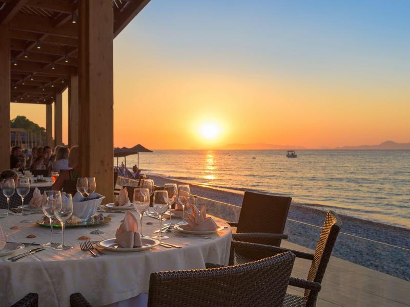 Terrassenrestaurant am Meer mit gedeckten Tischen, Sonnenuntergang und ruhigem Wasser im Hintergrund.
