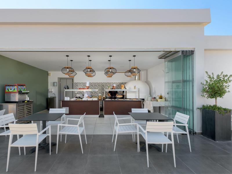 Moderner Außenbereich mit weißen Stühlen, Tischen und einer offenen Bar mit Hängelampen.