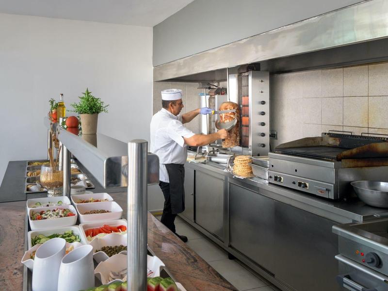 Professionelle Küche mit Koch vor großem Backofen und frischen Zutaten in Schalen auf Theke.