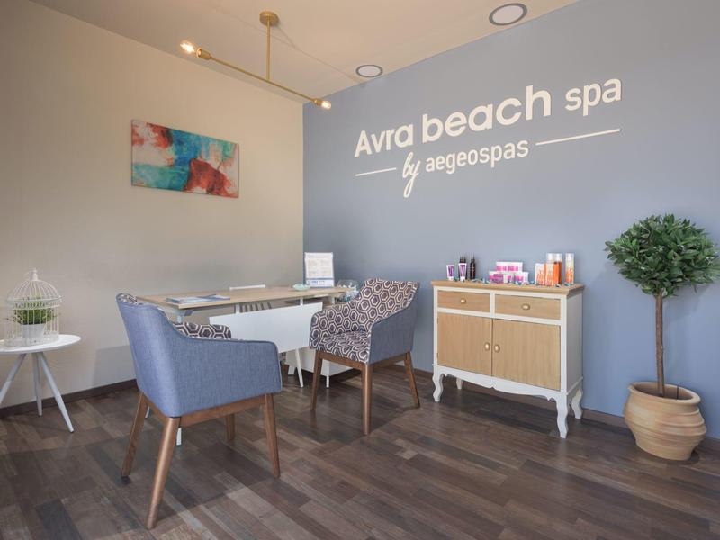 Heller Wellnessraum mit grauen Wänden, zwei Sesseln, Schreibtisch, Pflanze und Holzkommode.