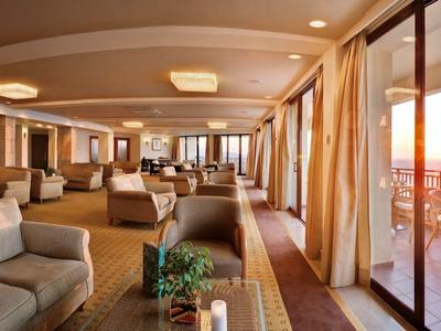 Geräumiger Lounge-Bereich mit Sofas und großer Fensterfront mit Blick auf Sonnenuntergang und Terrasse.