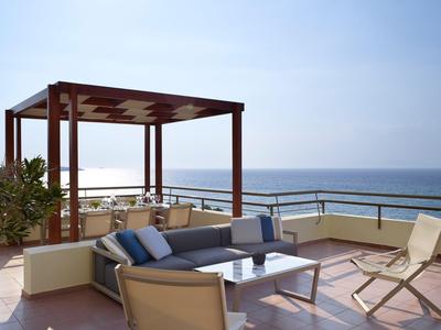 Terrace with lounge furniture and pergola overlooking the sea at a hotel.
