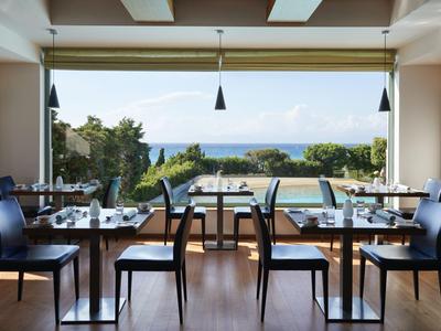 Modern dining room with view of pool, garden, and sea in the background in a hotel.