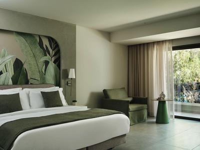 Modern hotel room with large bed, green armchair, and garden view.