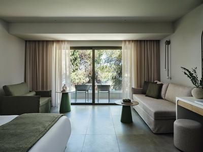 Modern hotel room with balcony, seating area, and view of trees.