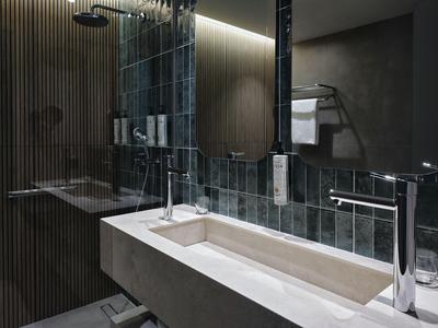 Modern hotel bathroom sink area with long basin and illuminated mirror.