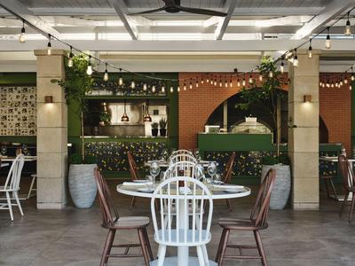 Cozy hotel outdoor area with tables, chairs, and green plants under a covered roof.