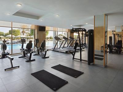 Modern hotel gym with exercise equipment and panoramic windows overlooking the outdoor area.