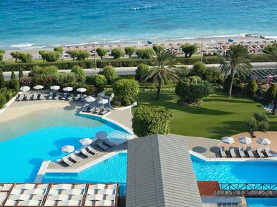 Blick auf Resort-Pool mit Liegestühlen, Palmen und Meer im Hintergrund