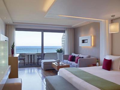 Bright hotel room with sea view, sofa, bed, and balcony seating area.
