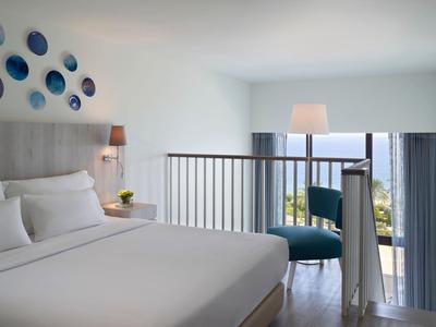 Bright hotel room with double bed, wall decoration, and lounge area with sea view.