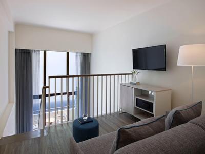 Bright living room with sofa, wall-mounted TV, floor lamp, and balcony view with railing.