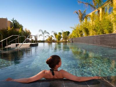 Person relaxes in clear pool water with views of palm trees and blue sky.
