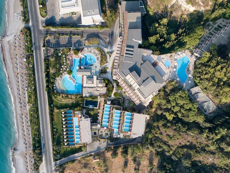 Aerial view of a resort with multiple pools, surrounded by trees and near the sea
