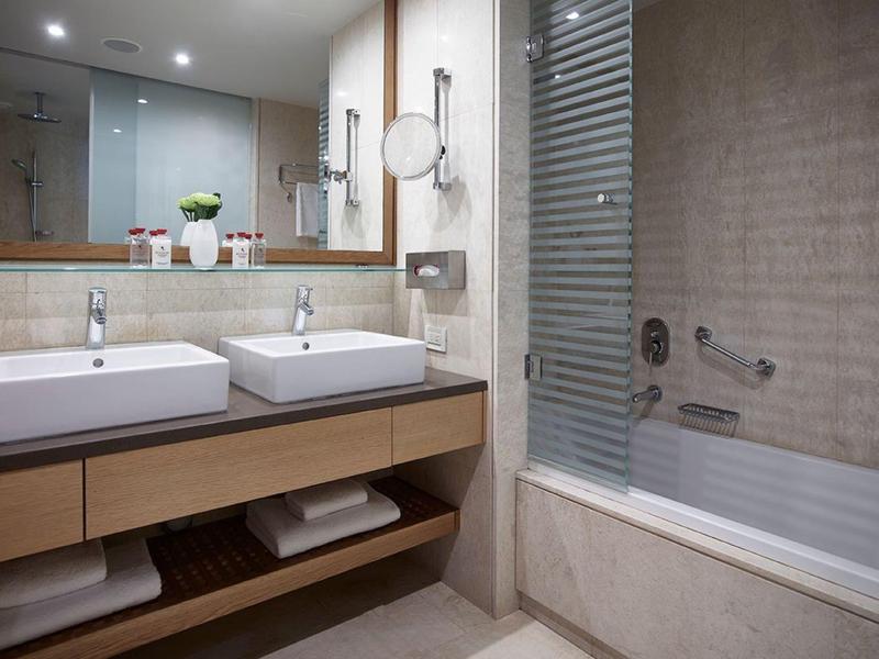 Modern bathroom with double sinks, large mirror, and bathtub with glass shower screen.