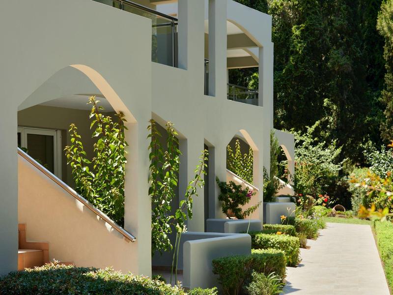 Modern building complex with white walls, garden, and sunlight on a walkway.