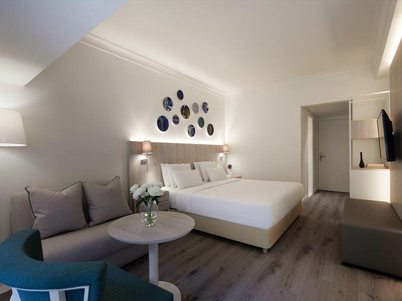 Modern hotel room with double bed, table, chairs, and wall decoration.